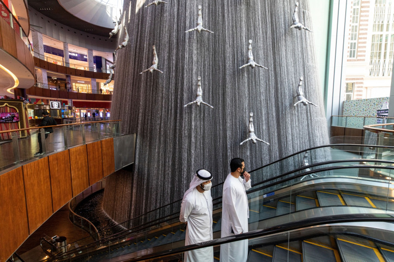 متسوّقان يرتديان قناعين واقيين يصعدان على سلم متحرك في مركز "دبي مول" للتسوق، دبي، الإمارات العربية المتحدة.