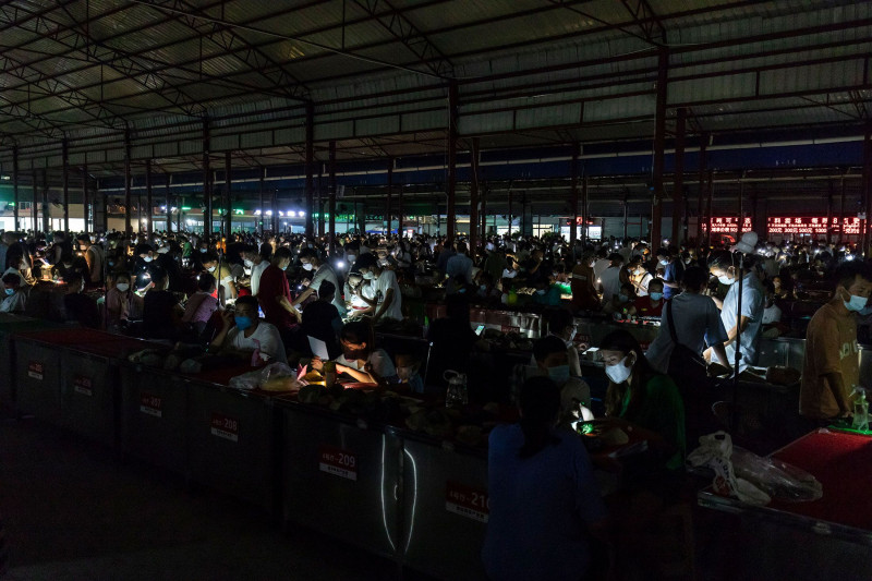 يضيء العملاء كشافات متخصصة لفحص الأحجار الخام في سوق ديلونغ الليلي.