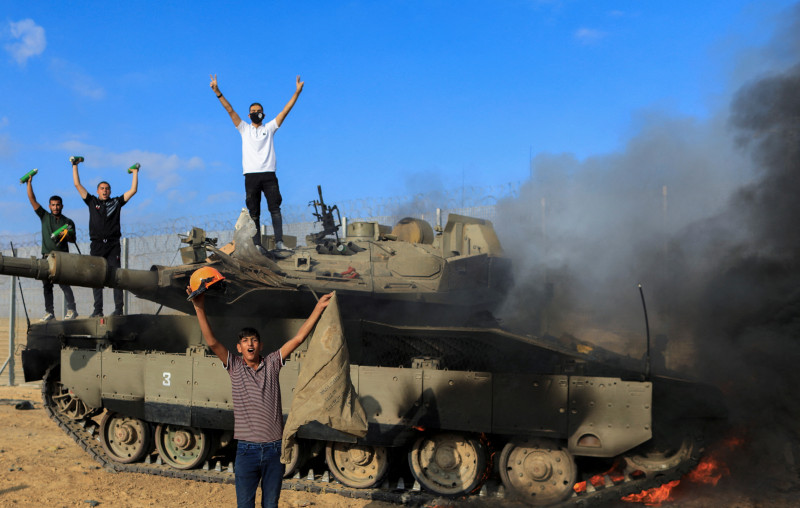 فلسطينيون يحتفلون بإحراق مركبة عسكرية إسرائيلية بعد استهدافها، على الجانب الإسرائيلي من الحدود بين إسرائيل وغزة، 7 أكتوبر، 2023