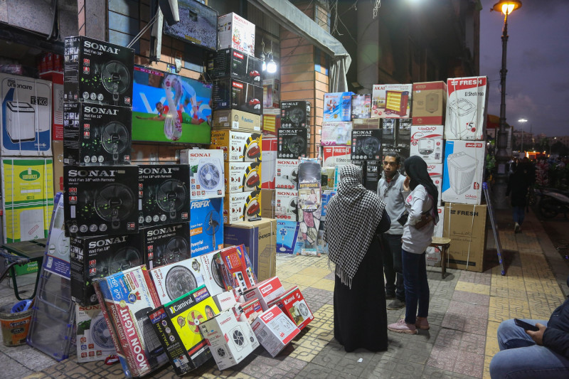 بائع يتحدث مع عميلتين خارج متجر إلكترونيات في سوق بالاسكندرية، مصر.