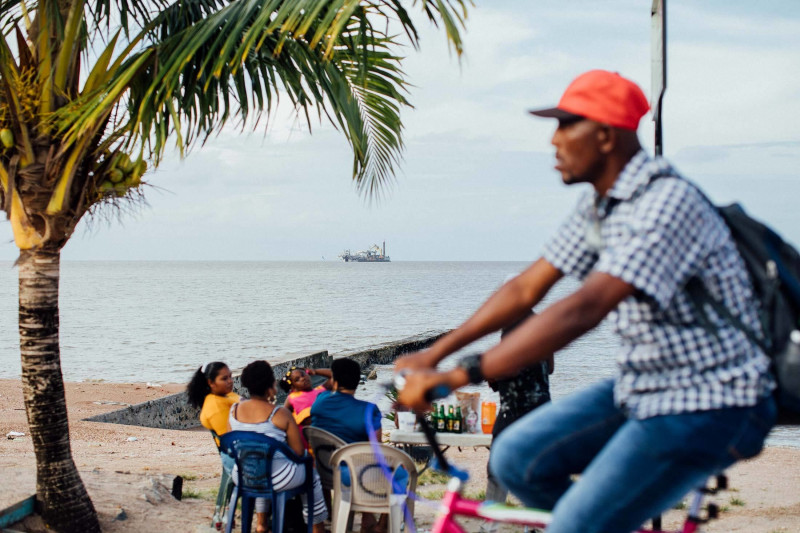 مواطنون يجلسون على الجدار الشاطئي في جورج تاون فيما تبحر ناقلة نفط قبالة ساحل غيانا