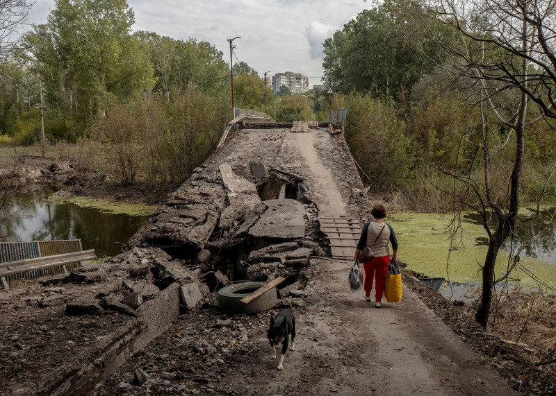 امرأة أوكرانية تعبر جسراً دمره الجيش الروسي بعد انسحابه من مدينة بالاكليا بمقاطعة خاركيف سبتمبر الماضي.